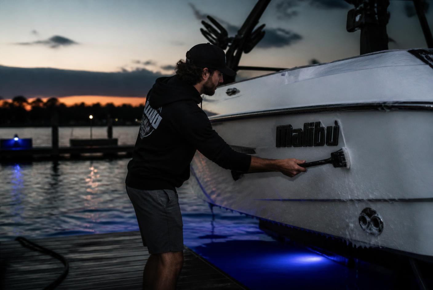 Blue Mobile Detailing technician scrubbing a wake boat hull dockside at Lake Travis near Austin, TX