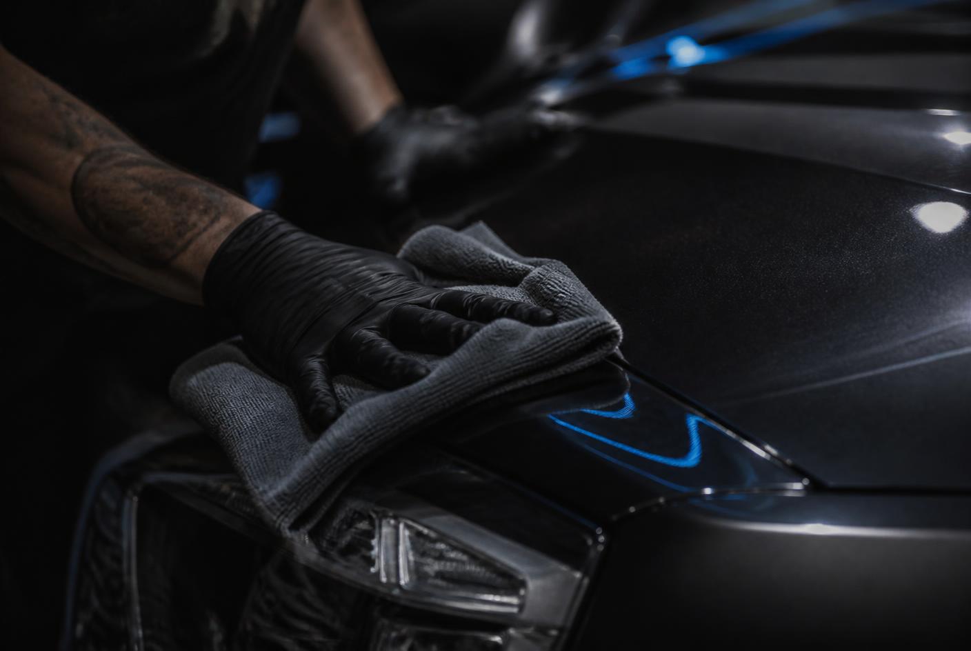 Blue Mobile Detailing technician wiping down glossy dark car paint with a microfiber towel in Austin, TX